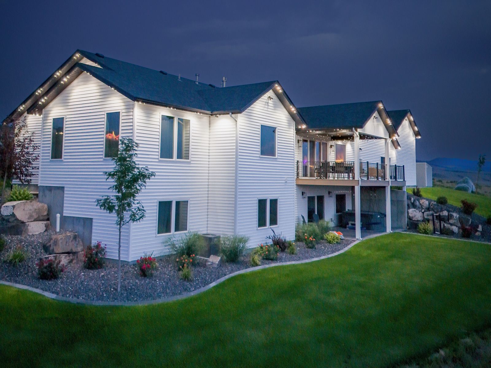 Home at dusk with warm white accent lighting along the rooflines and a lit back deck